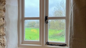 A room with a white-framed window overlooking a green field and trees. - Meadow View Cottage (Cheltenham)