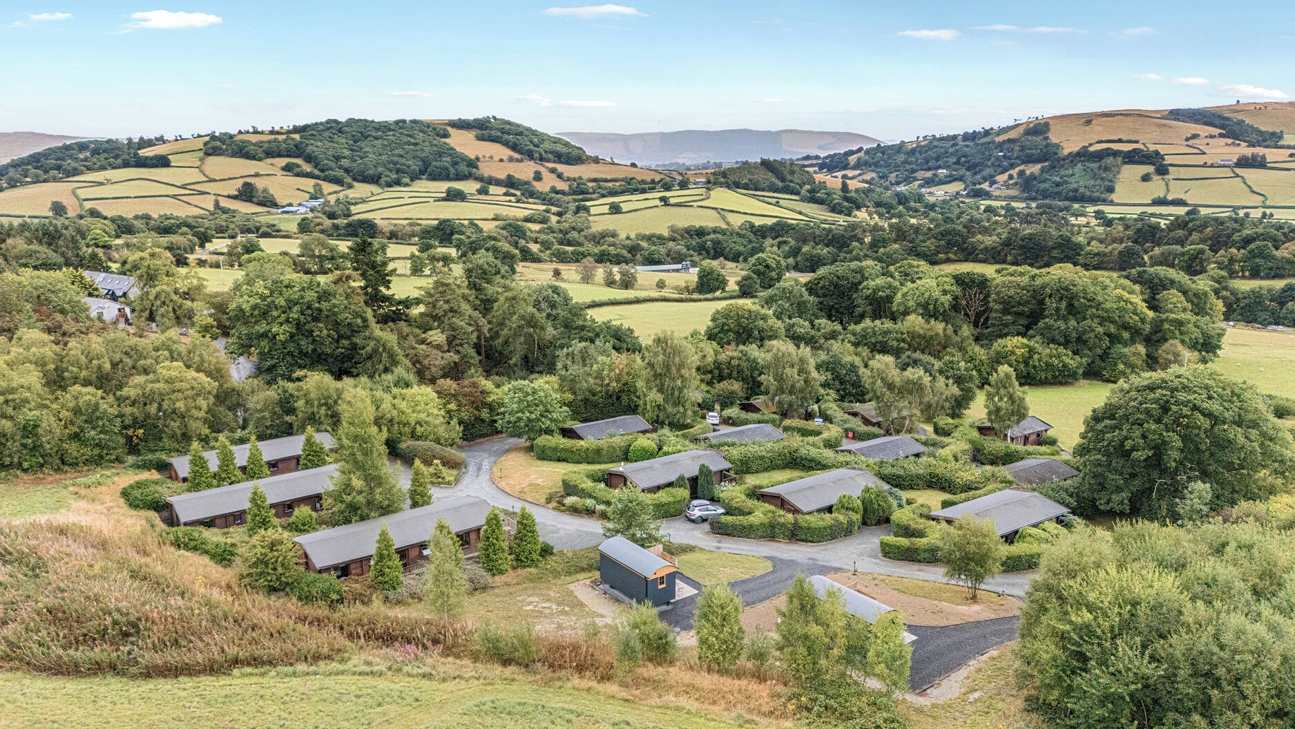 Zona residencial rural con varias casas, rodeada de abundante vegetación y colinas ondulantes.
