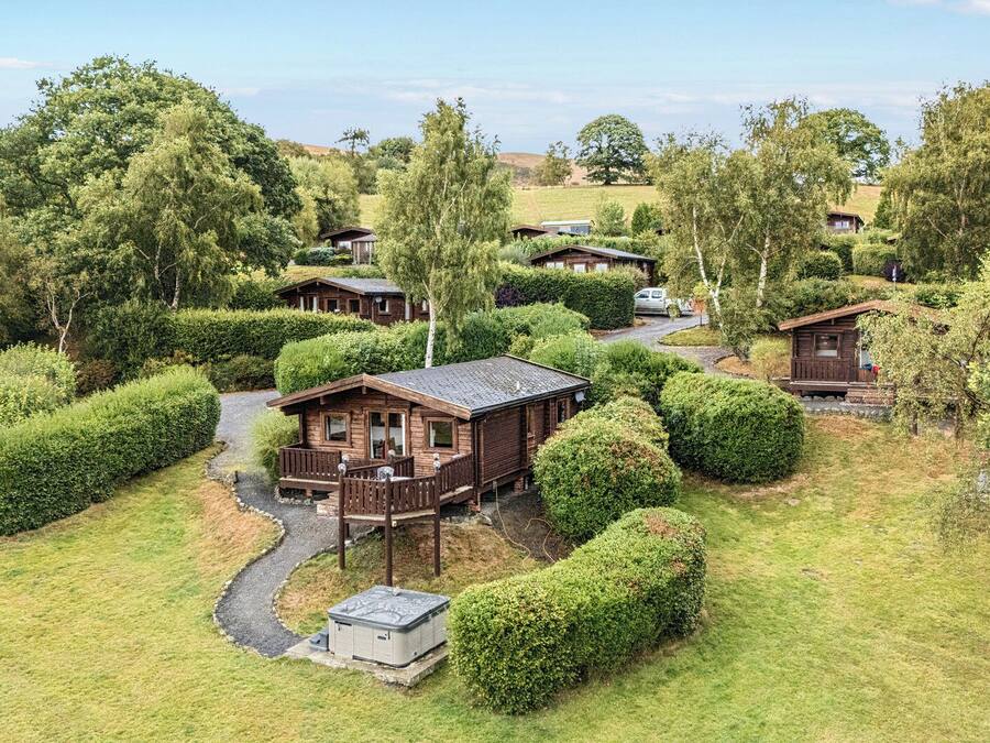 A cluster of wooden cabins surrounded by well-maintained hedges and trees, with a gravel path connecting them.