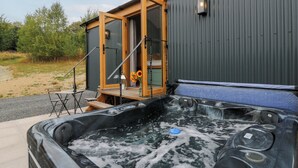 Ein Whirlpool mit einer Holzterrasse und einer Glasumrandung, an ein Gebäude angebaut.