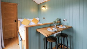 Ein gemütliches Zimmer mit einem Bett, einem kleinen Tisch mit zwei Hocker und einer Wandleuchte.