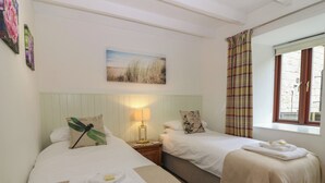 Ein Hotelzimmer mit zwei Betten, einem Nachttisch mit Lampe, einem Bild an der Wand und einem Fenster mit Vorhängen.