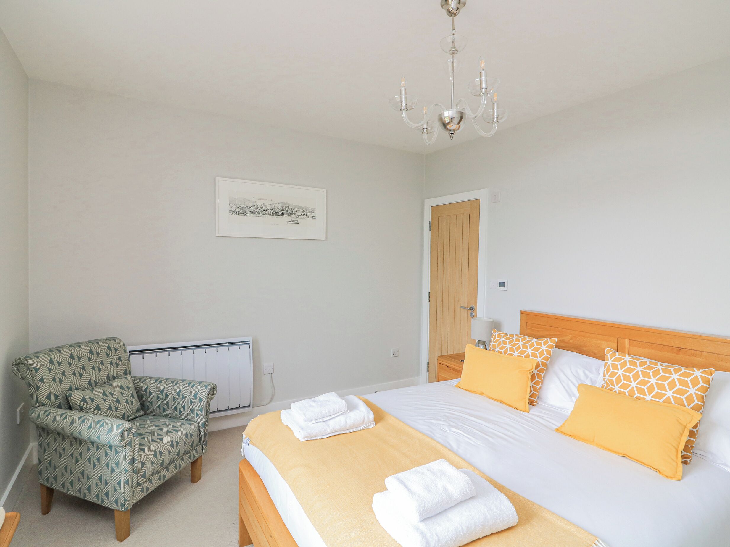A bedroom with a bed, a chair, a radiator, a door, and a chandelier.