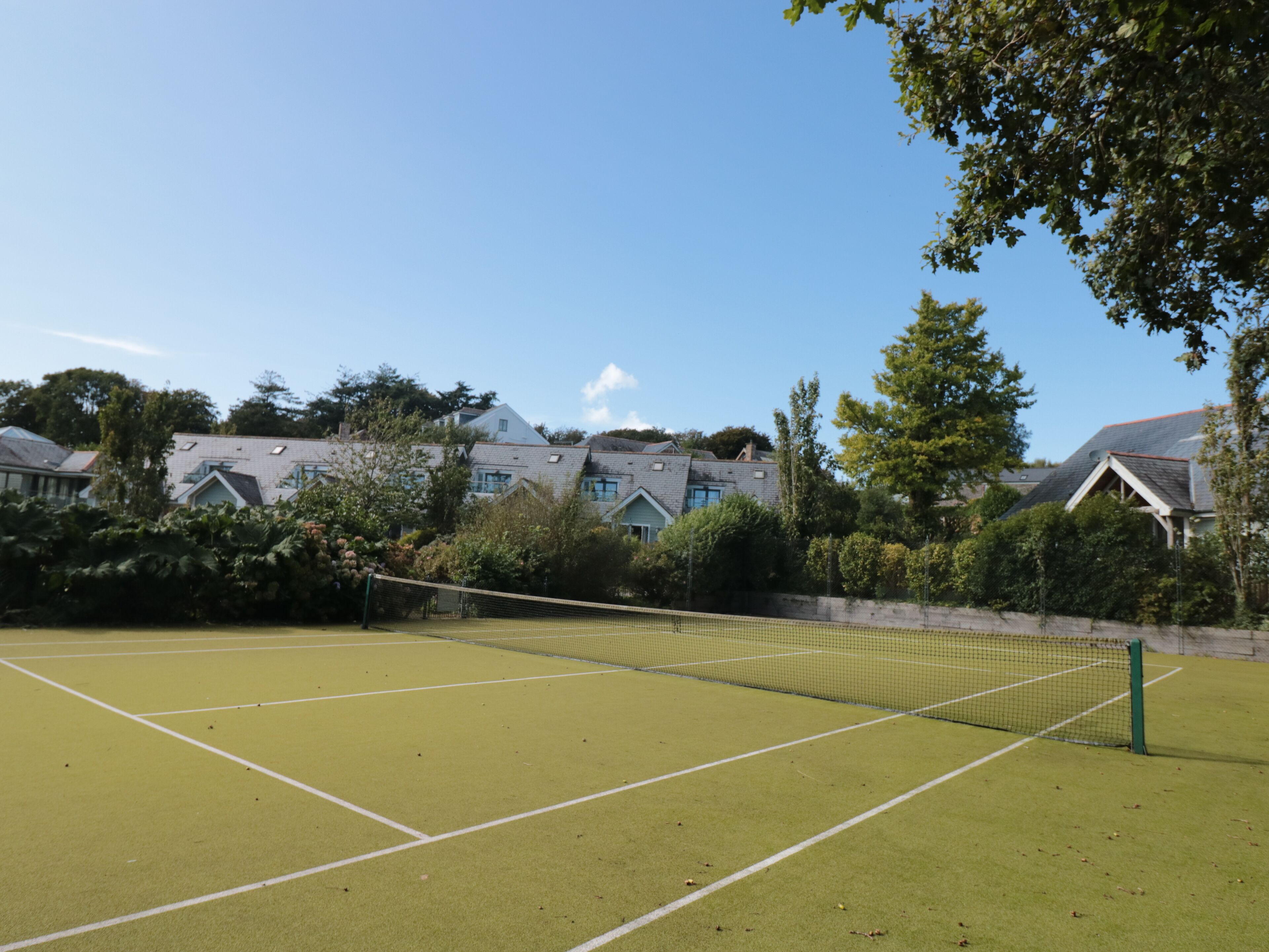 A tennis court with a net, surrounded by houses and trees.