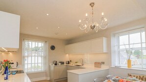 A modern kitchen with white cabinetry, a central island, and a dining area with a glass table set for six. - 4 The Manor House Hillfield Village (Dartmouth)