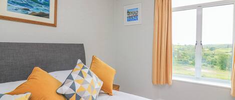 A hotel room with a bed, a window with curtains, a framed painting, and a small picture on the wall.