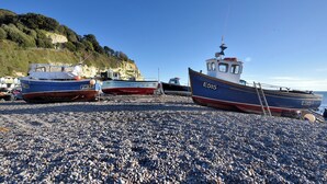 Boats docked on a pebbled beach with a cliff in the background. - Pebble Beach Chalet (Seaton)