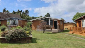 A row of log cabins with a grassy yard and a clear sky. - Pebble Beach Chalet (Seaton)
