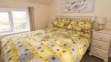 Un dormitorio con cama, mesita de noche, lámpara y ventana.