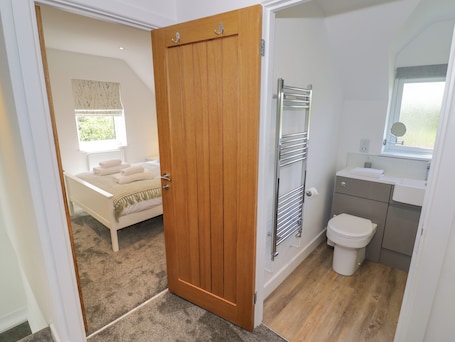 A bedroom with a bed, a bathroom with a toilet, and a wooden door.. Ranch Cottage
