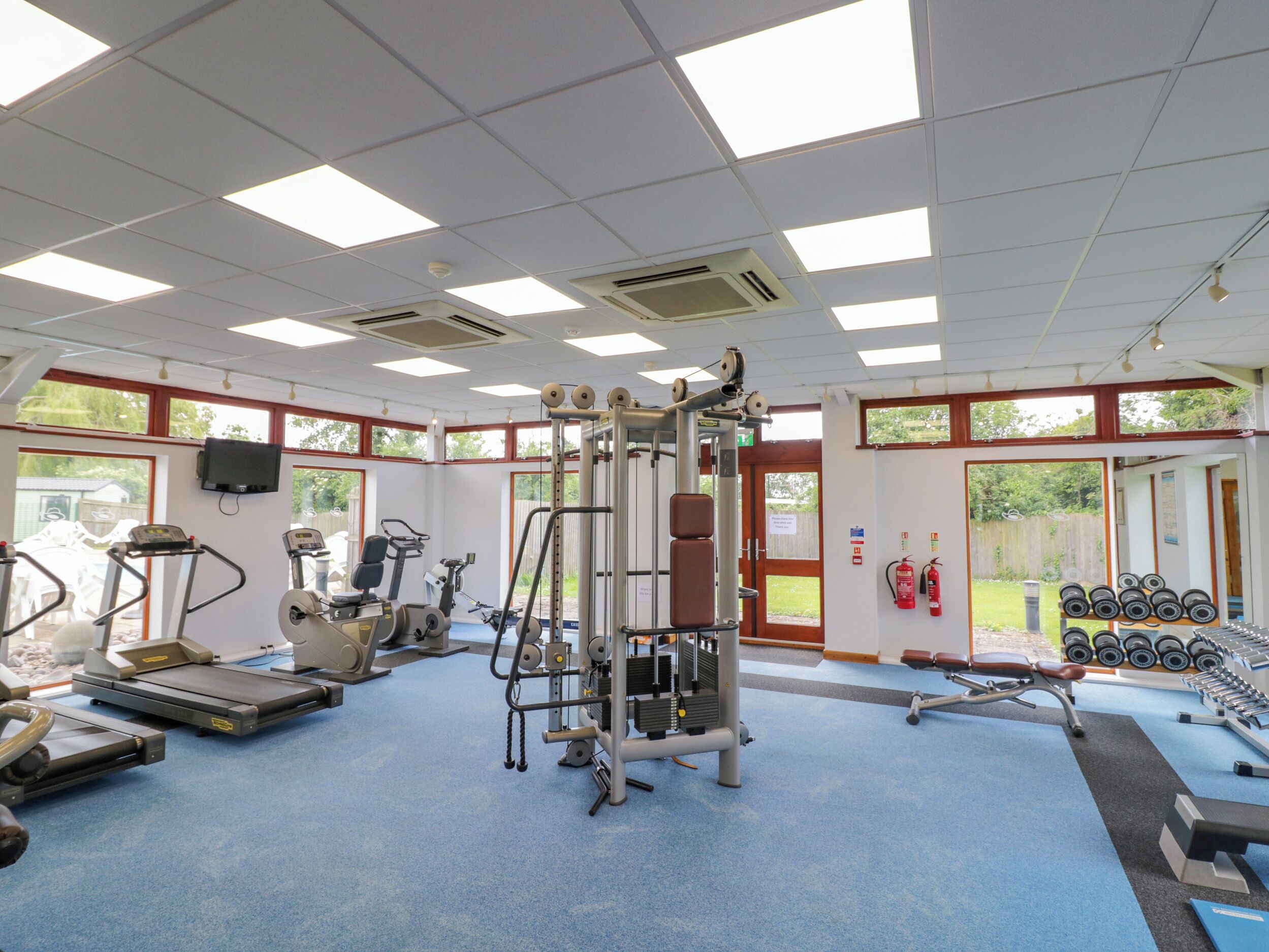 Ett gym med träningsutrustning, en blå matta och stora fönster.