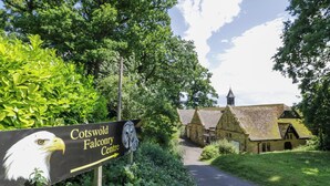 A sign for Cotswold Falconry Centre with a pathway leading to traditional stone buildings.