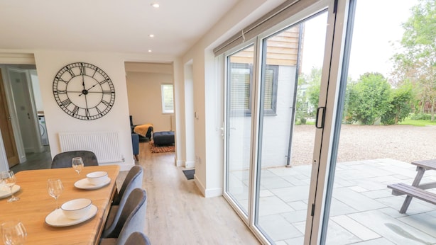 A dining area with a large table set for four, a wall clock, and a view of the outdoor patio.