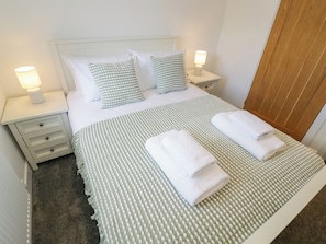 A neatly made bed with a checkered bedspread and pillows, two bedside lamps, and a wooden door.