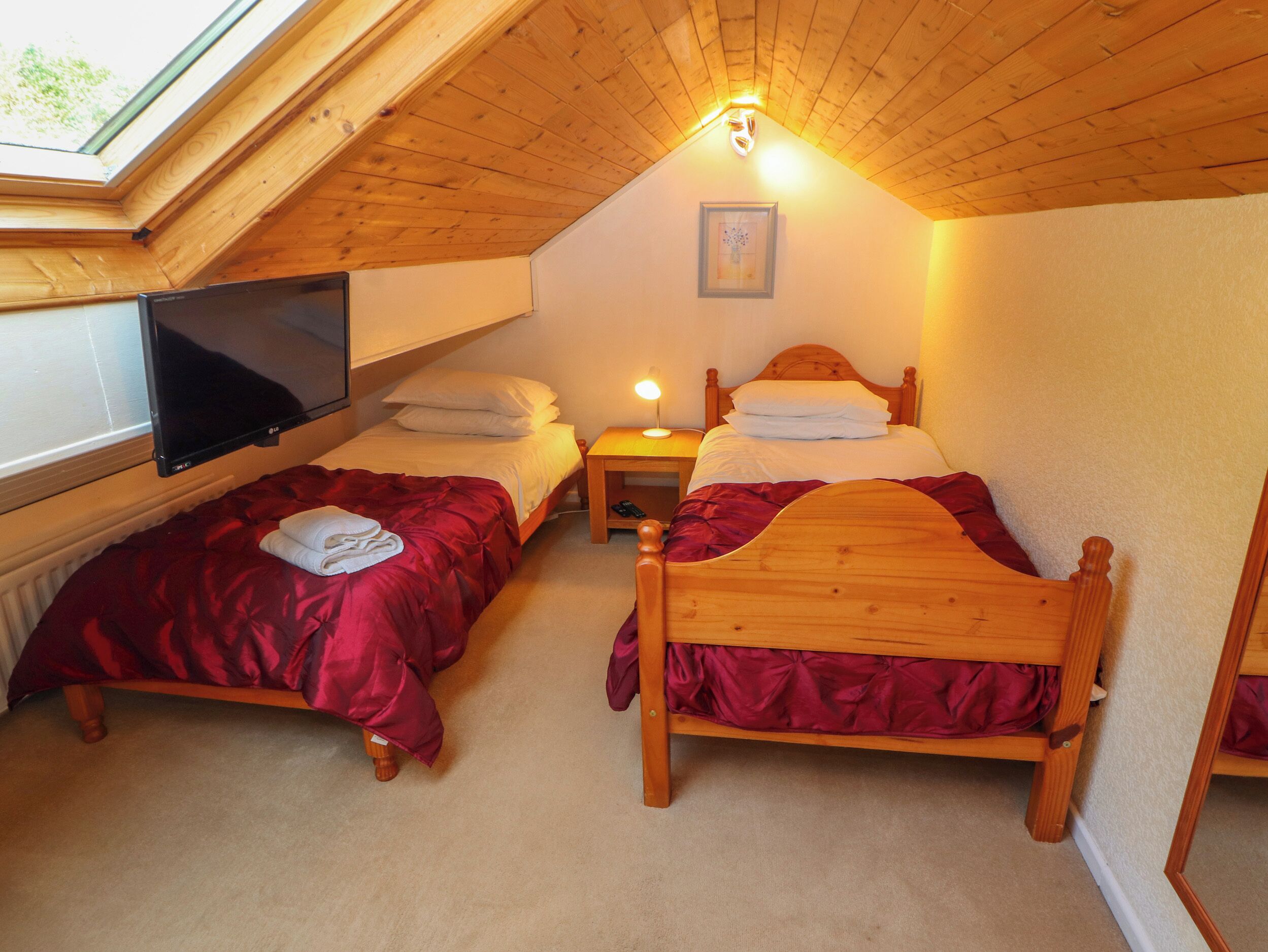 A cozy attic bedroom with two wooden beds, a television, and a skylight.