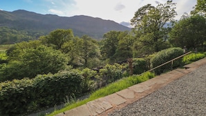 A stone pathway leading through a lush green landscape with trees and a mountain in the background.