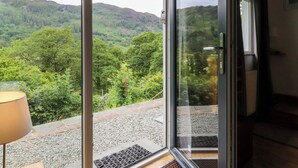 A room with a large glass door leading to a scenic outdoor view of a forested hillside.