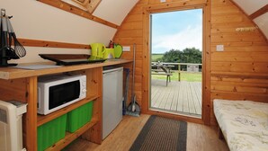 A compact, wooden cabin-style room with a kitchenette, a bed, and a large window overlooking a grassy area. - Sheep Shed @ Penbugle Organic Farm (Liskeard)