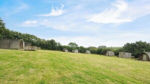 A grassy field with several small wooden cabins and a larger building with a porch. - Sheep Shed @ Penbugle Organic Farm (Liskeard)