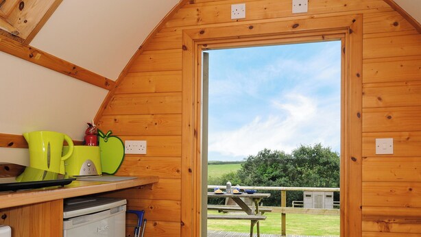 A wooden interior with a kitchen area, a dining table outside, and a view of the countryside. - Sheep Shed @ Penbugle Organic Farm (Liskeard)