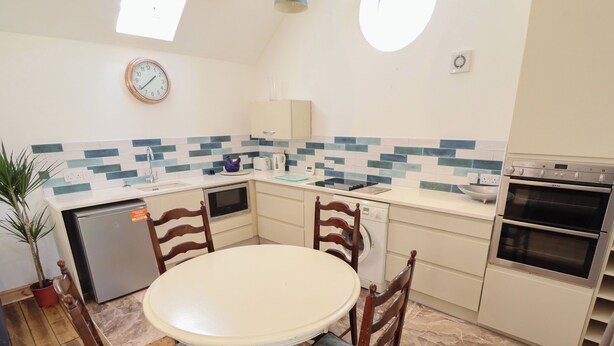 A compact kitchen with a round dining table, wooden chairs, a built-in oven, and a microwave. - The Stable (Boston)