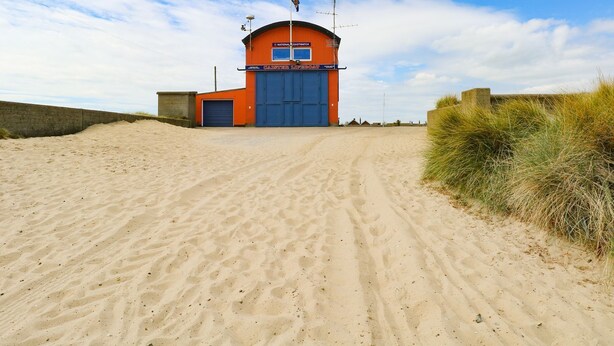 A coastal building with a large blue door, a small window, and a flag on top. - Flint Cottage (Great Yarmouth)