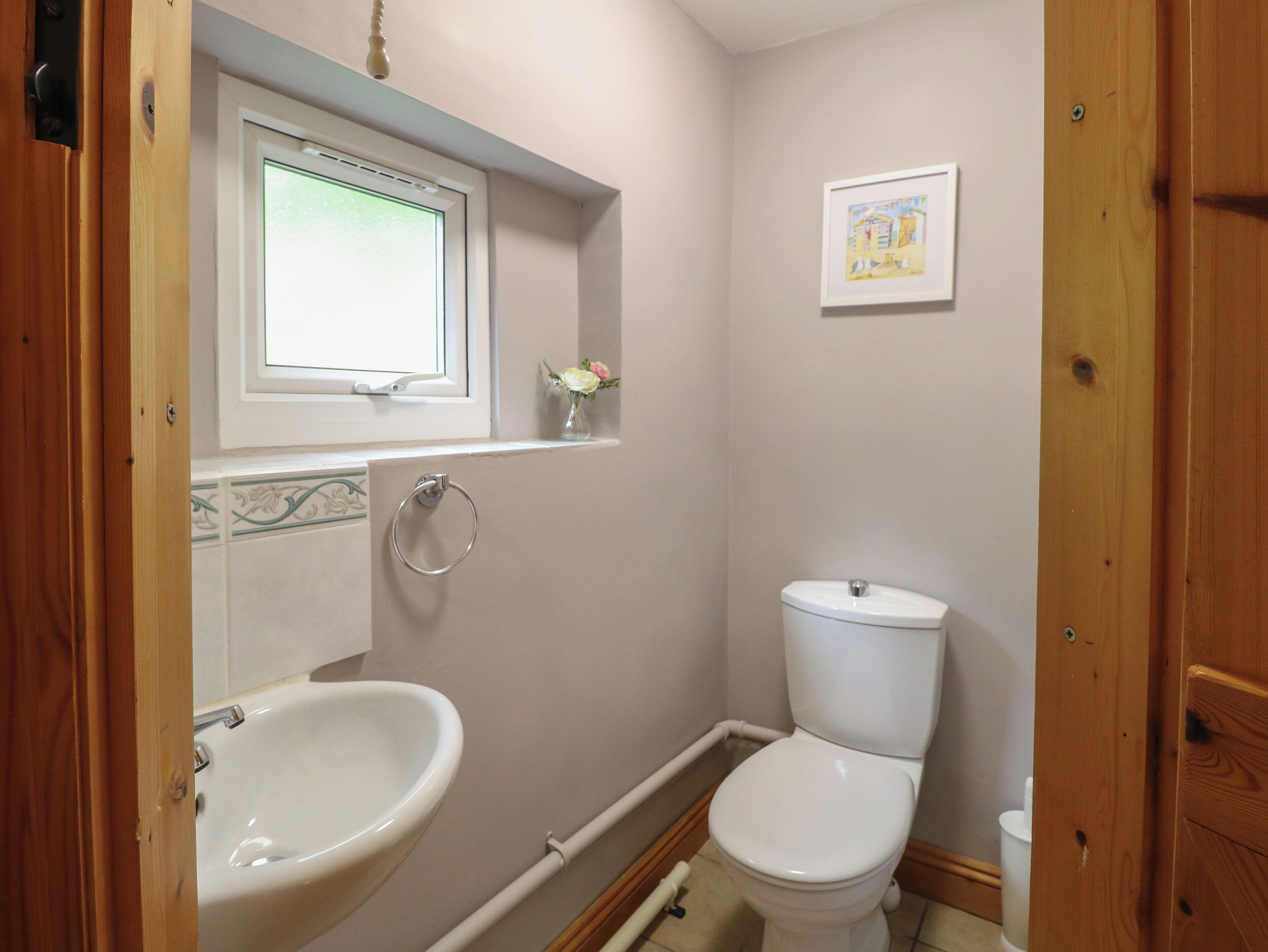 Een kleine badkamer met een wit wastafel, toilet en een raam boven de wastafel.