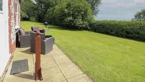 A patio with wicker furniture, a barbecue grill, and a well-maintained lawn. - Flint Cottage (Great Yarmouth)