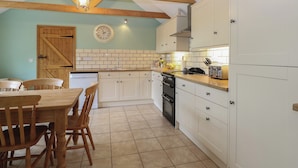 A kitchen with wooden beams, white cabinets, a tiled backsplash, and a dining area with wooden chairs. - Flint Cottage (Great Yarmouth)
