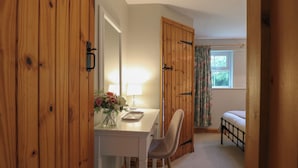 A bedroom with a wooden door, a desk with a lamp, a chair, a bed, and a window with curtains. - Flint Cottage (Great Yarmouth)