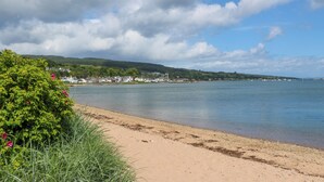 A coastal landscape with a sandy beach, a calm sea, and a town in the background. - Lodge 3 - "beech" (Isle of Arran)