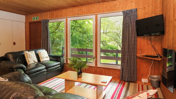 A cozy room with a leather sofa, a wooden coffee table, and a TV mounted on the wall. - Lodge 3 - "beech" (Isle of Arran)