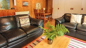 A cozy living room with two leather sofas, a wooden coffee table, and a fern plant. - Lodge 3 - "beech" (Isle of Arran)