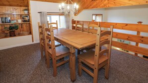 A wooden dining room with a large table and chairs, a chandelier, and a bookshelf with books and a plant. - Igamogam (Caernarfon)