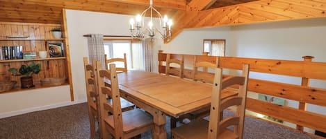 Uma sala de jantar de madeira com uma mesa grande e cadeiras, um lustre e uma estante de livros com livros e uma planta.