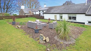 A residential property with a garden area featuring outdoor furniture, a stone wall, and a variety of plants. - Igamogam (Caernarfon)