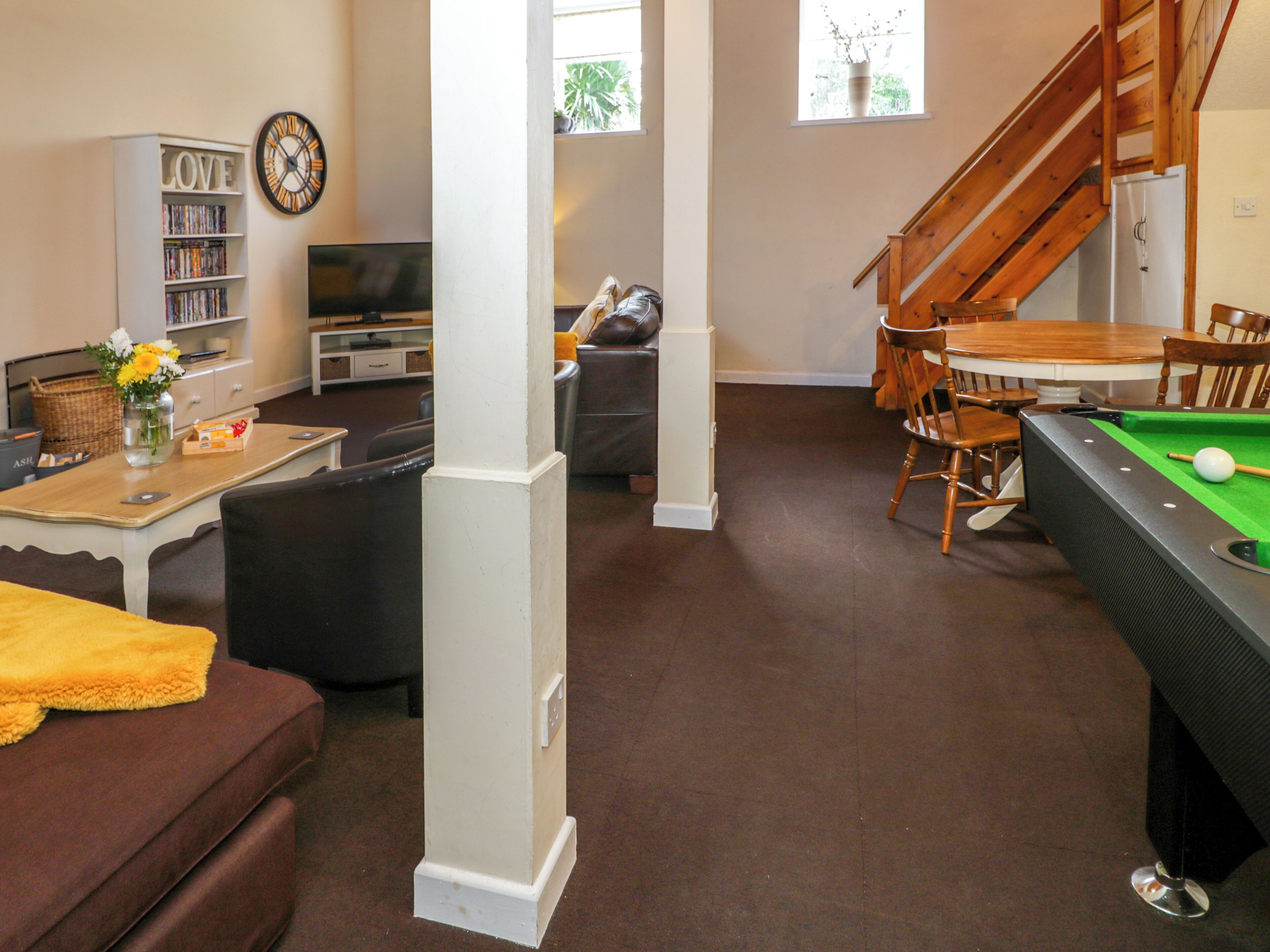 A living room with a pool table, a sofa, a coffee table, a bookshelf, and a staircase.