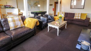 A cozy living room with a brown leather sofa, a wooden coffee table, and a brown sofa with yellow cushions. There is a pool table in the background and a map on the wall. - Igamogam (Caernarfon)