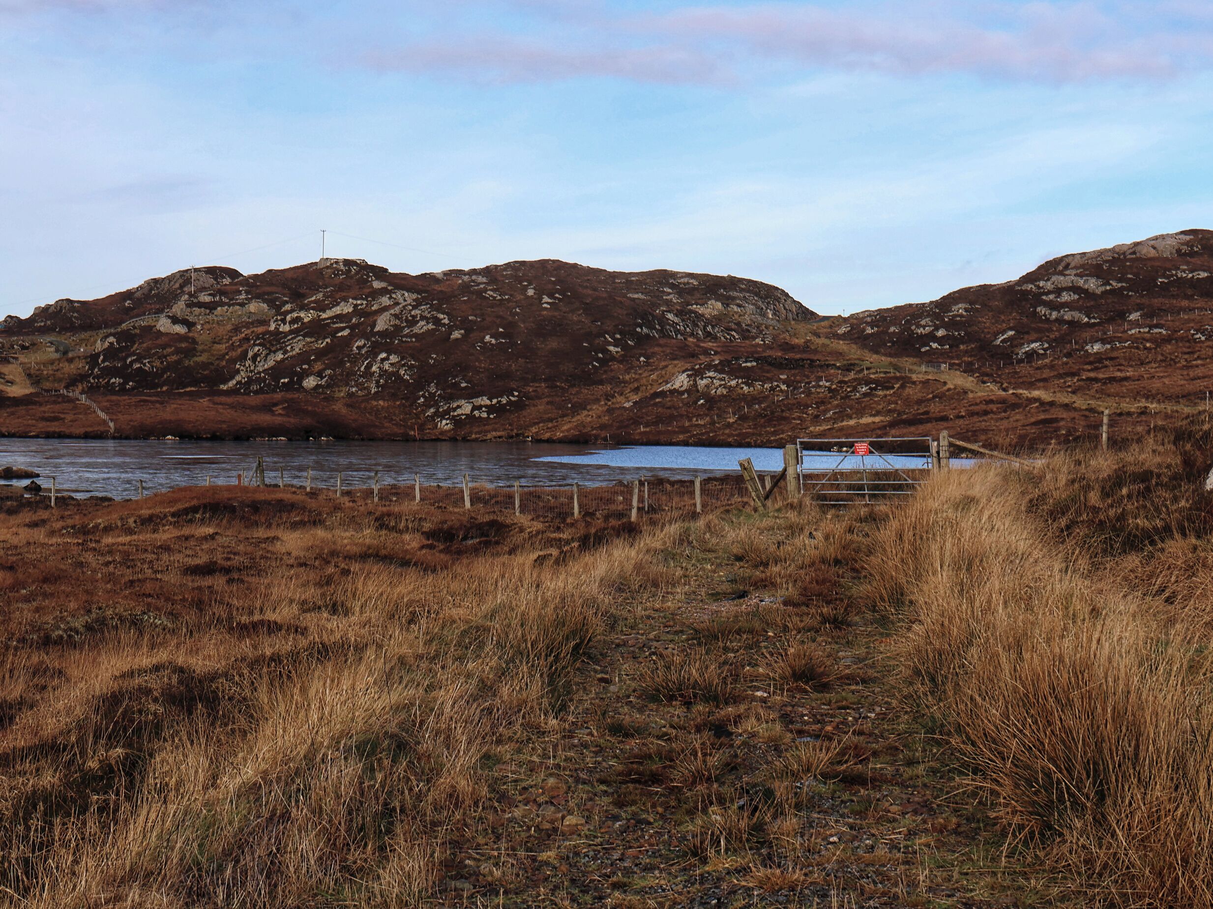 A rural landscape with a river, grassy fields, and rocky hills.