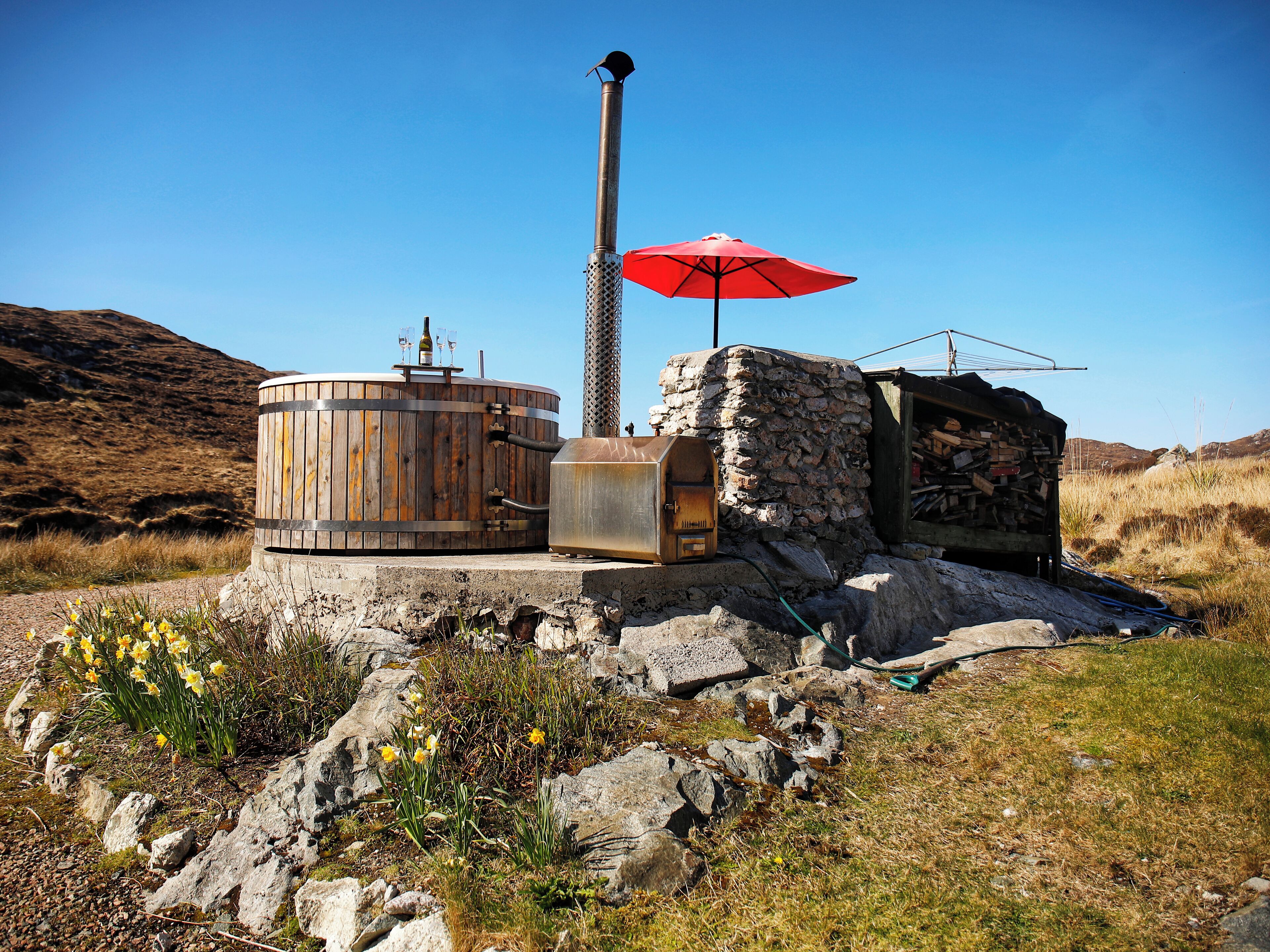 A rustic outdoor setting with a wooden barrel, a stone structure, and a red umbrella.