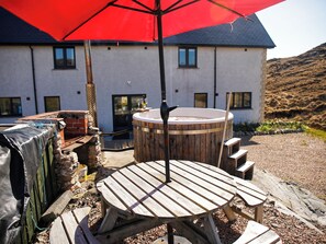 A wooden outdoor seating area with a hot tub, a red umbrella, and a building in the background.