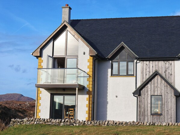 A two-story house with a balcony, a stone wall in front, and a wooden fence.