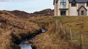 A modern house with a large glass balcony overlooking a rural landscape with a stream. - Riverside (Harris)