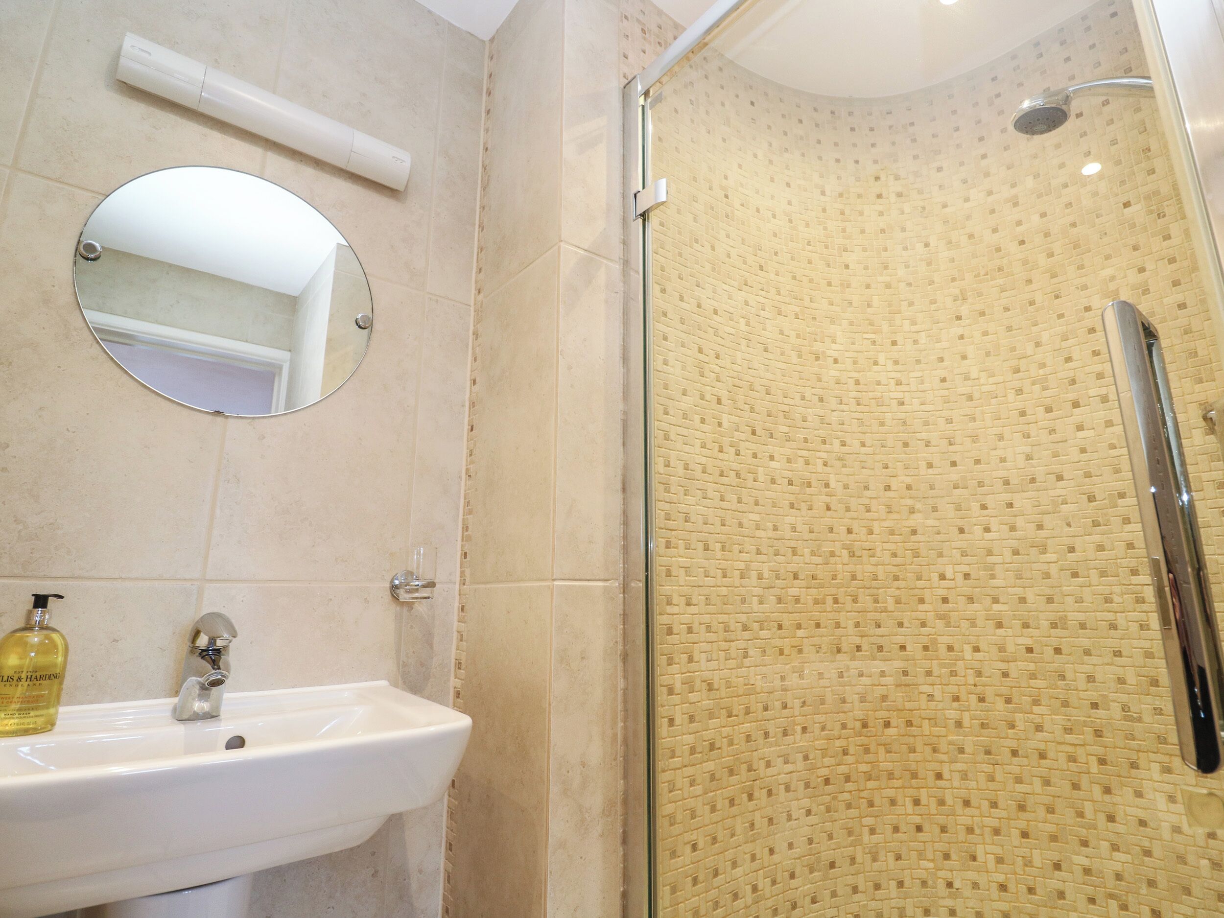 A bathroom with a sink, mirror, and shower.