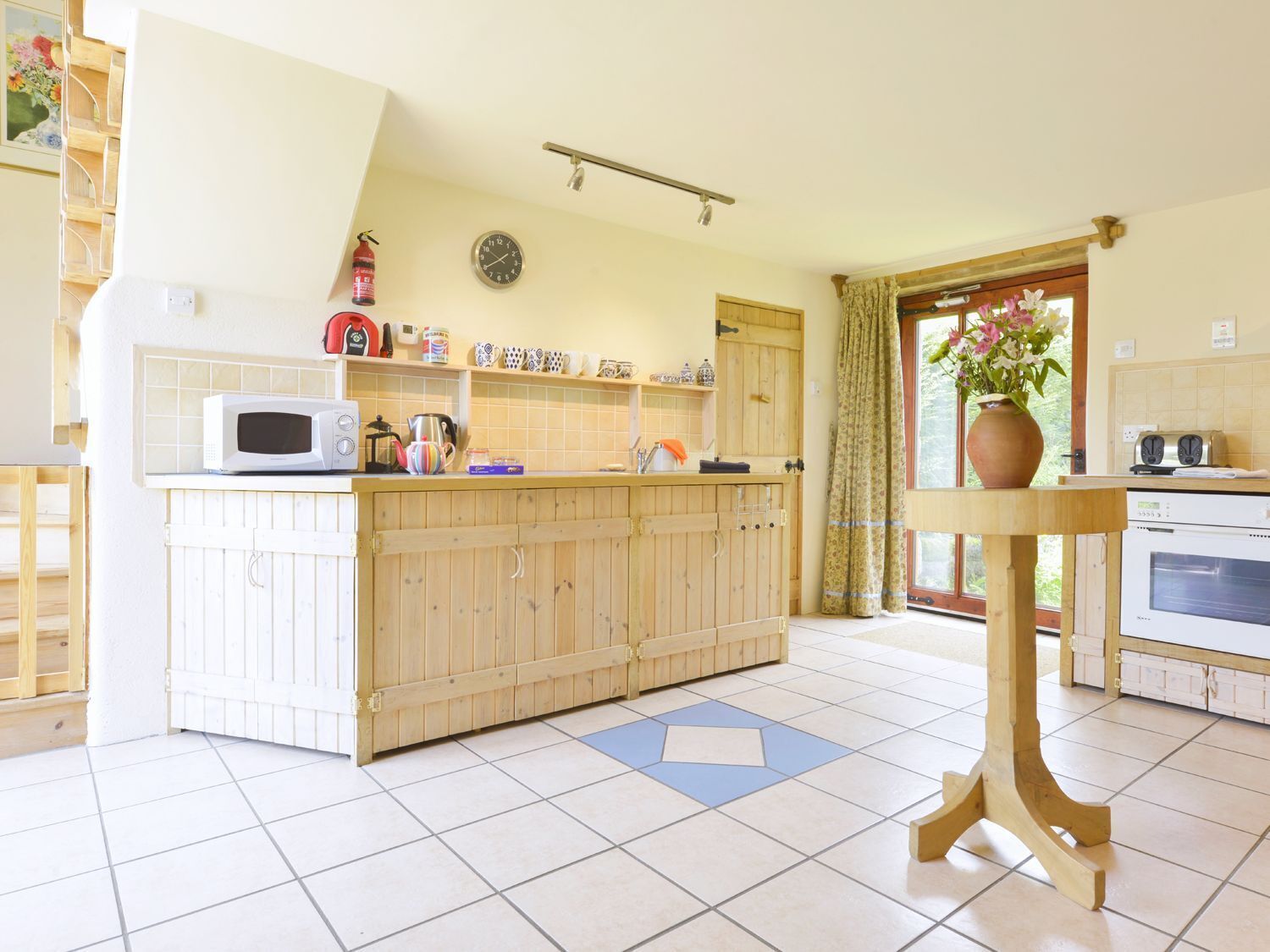 Una cocina con una isla de madera, microondas, tetera y un reloj en la pared.
