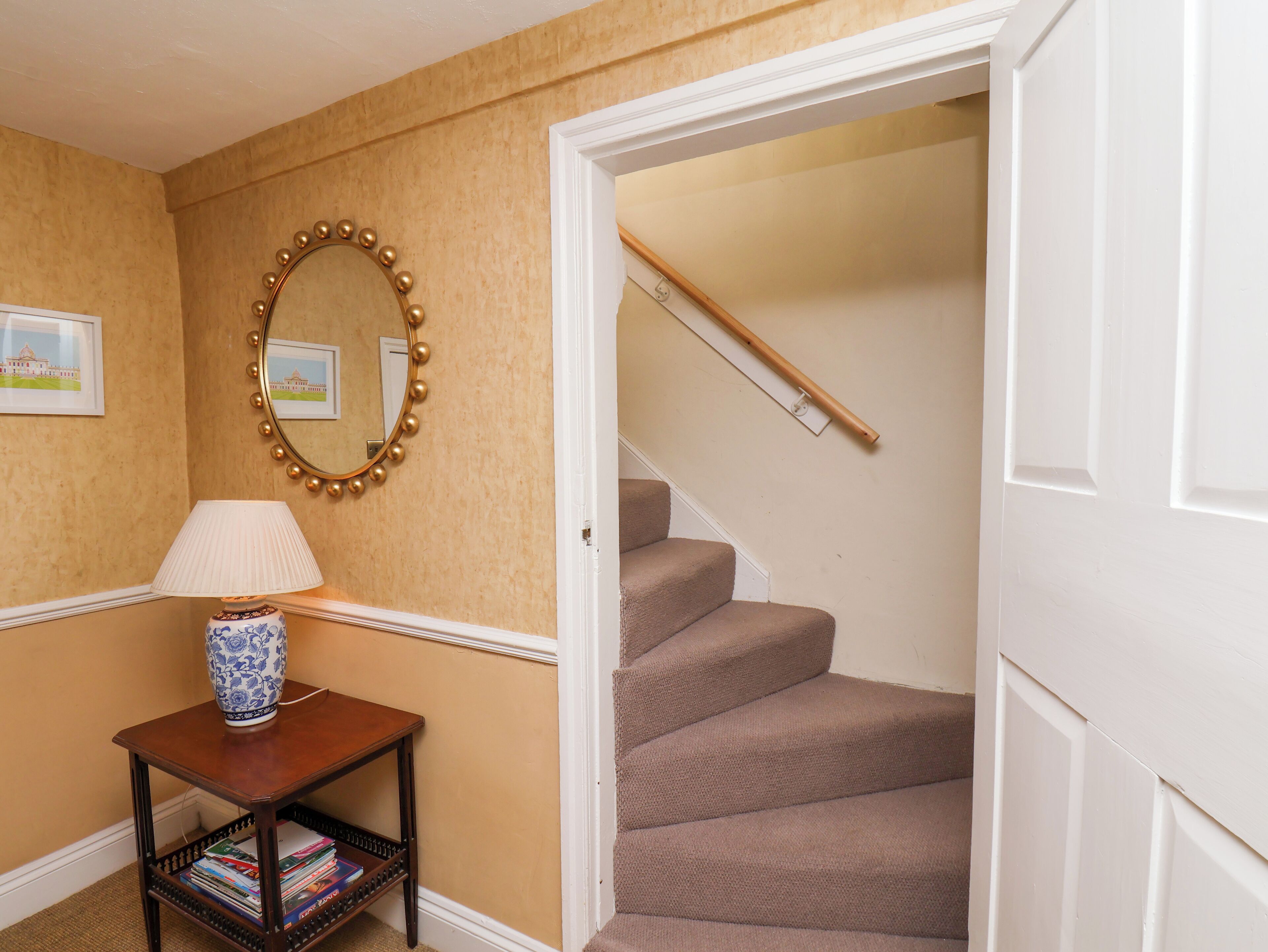A hallway with a lamp, a mirror, and a staircase.