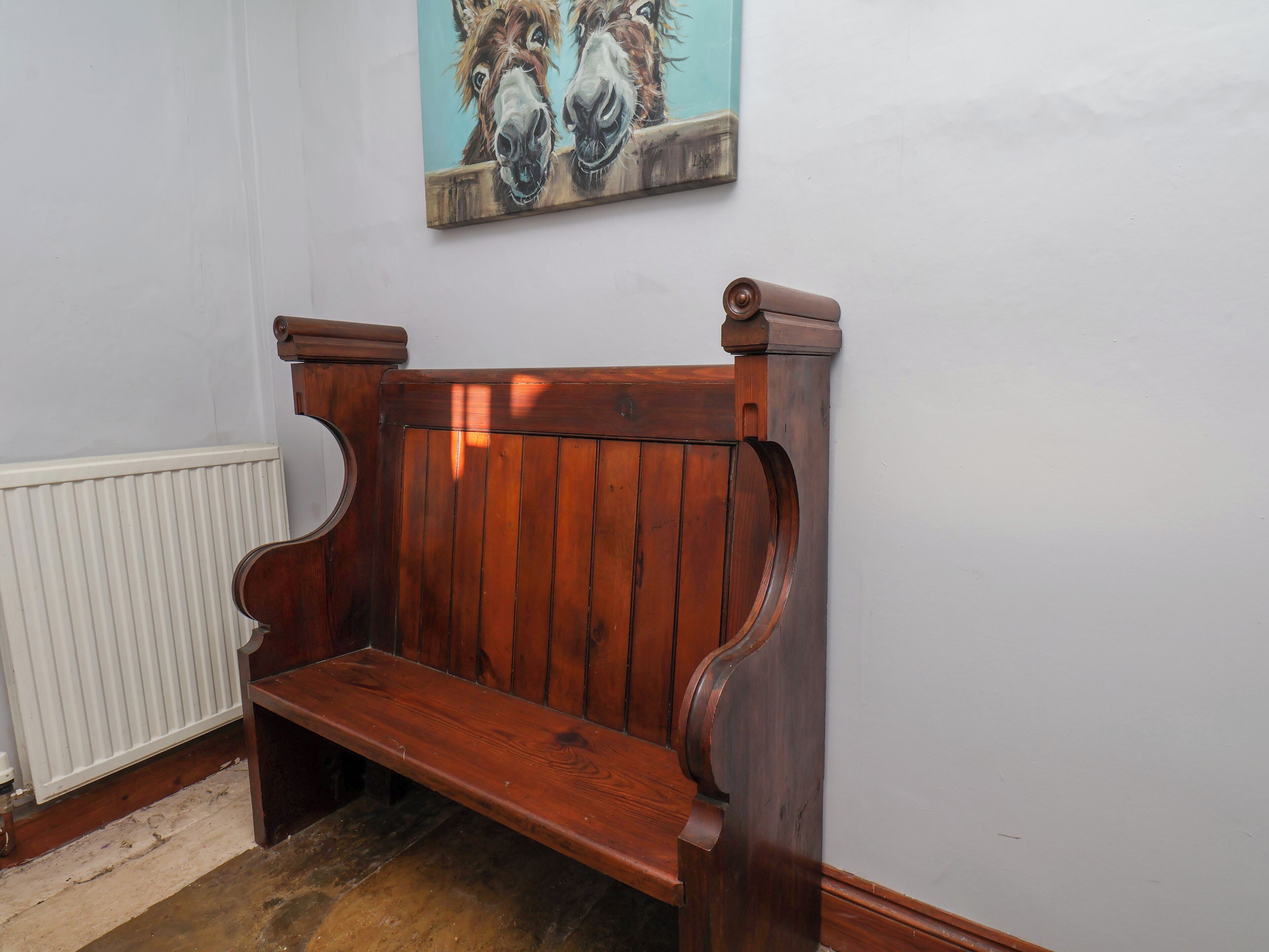 A wooden bench with a white radiator and a painting of horses on the wall.