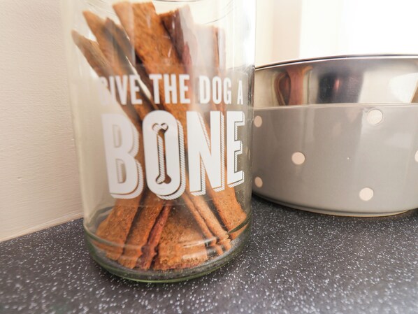 A glass container labeled "BONE" with cinnamon sticks inside, next to a gray bowl with white polka dots.
