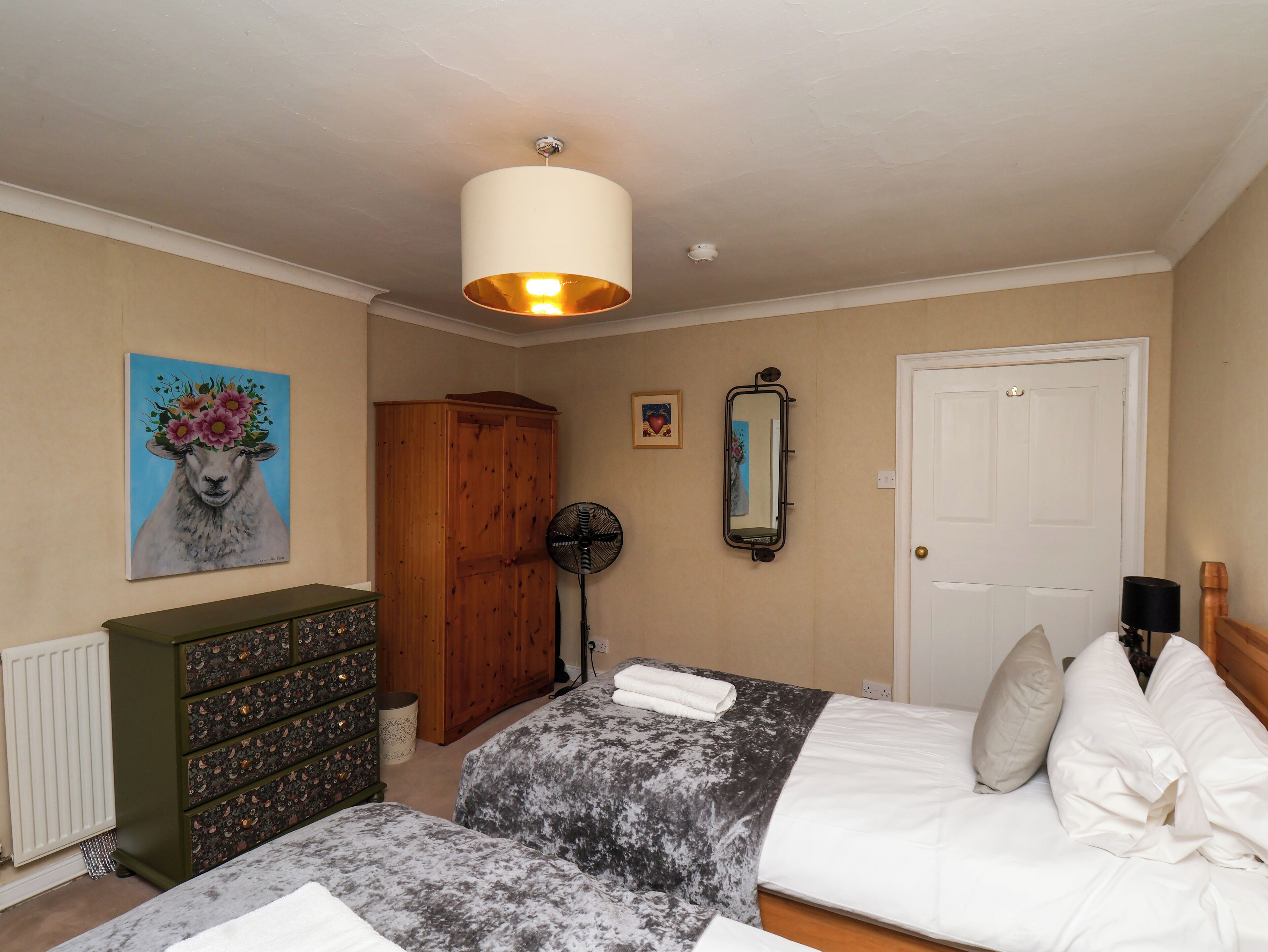 A bedroom with a bed, dresser, and a painting of a sheep on the wall.