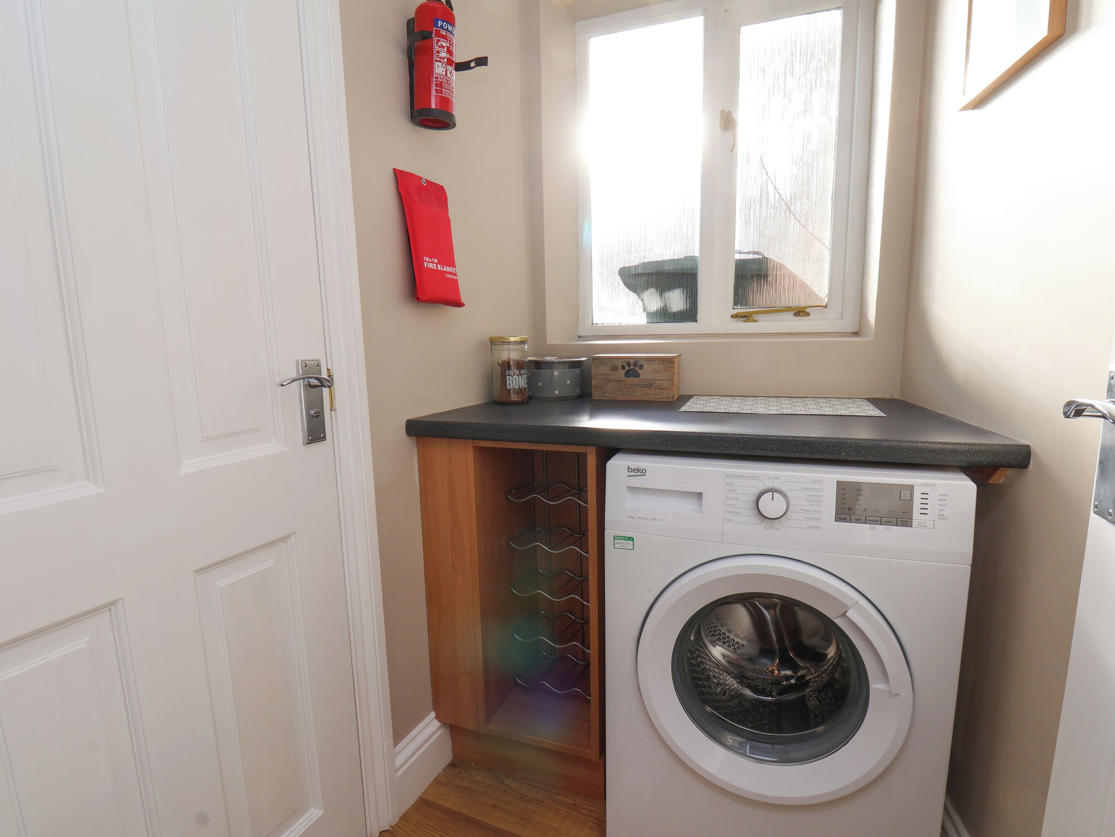 A compact laundry room with a washing machine, a fire blanket, and a fire extinguisher on the wall.